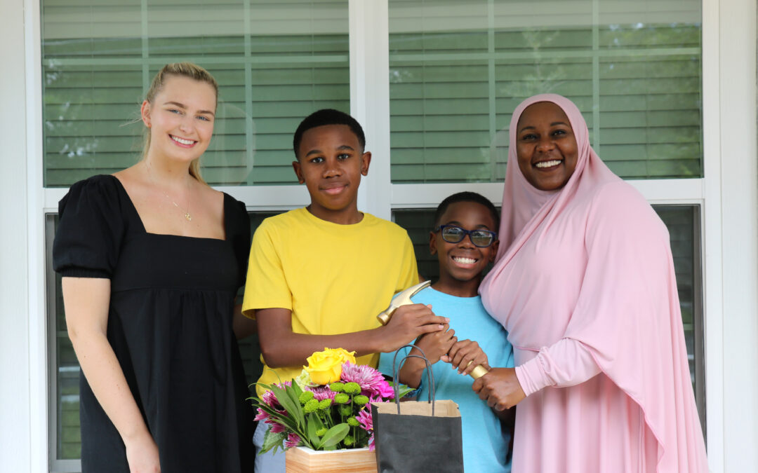 Two women stand on either side of two boys, who hold a golden hammer.