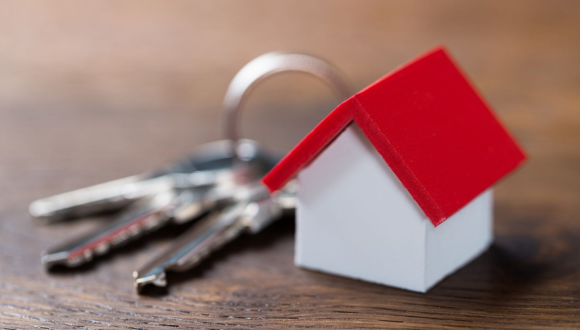 A white house with a red roof sits next to a set of keys.