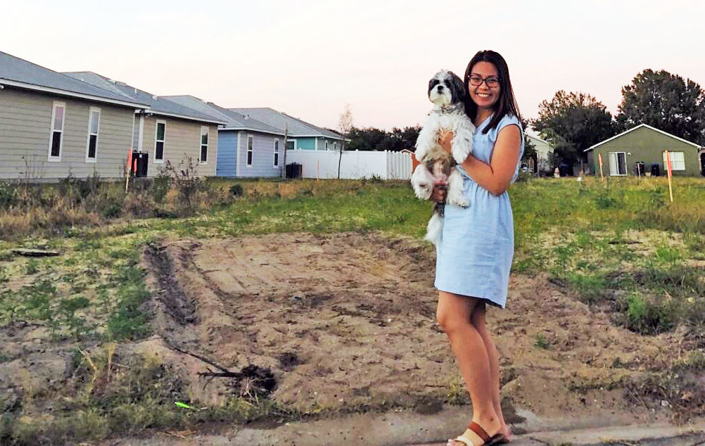 woman stands with her dog at dirt lot where her home will be built