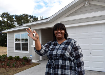A smiling woman holds up her keys in front of her home.