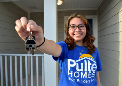 A smiling woman poses with house keys in front of her home.