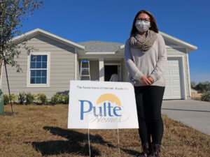 Uma mulher está ao lado de uma placa que diz: &quot;A futura casa de Hannah graças à Pulte Homes&quot;