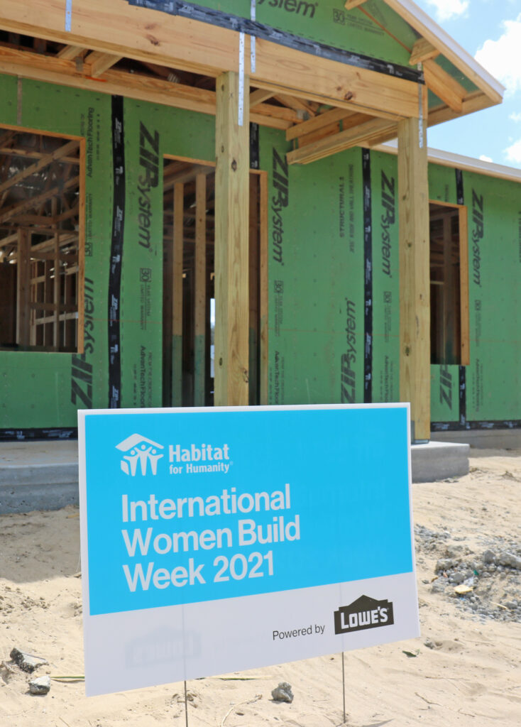 mujeres construyen un cartel delante de una casa en construcción