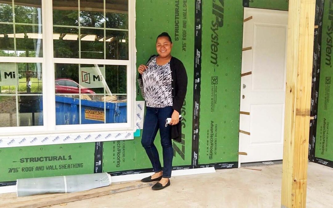 A woman standing in front of a house under construction smiles at the camera