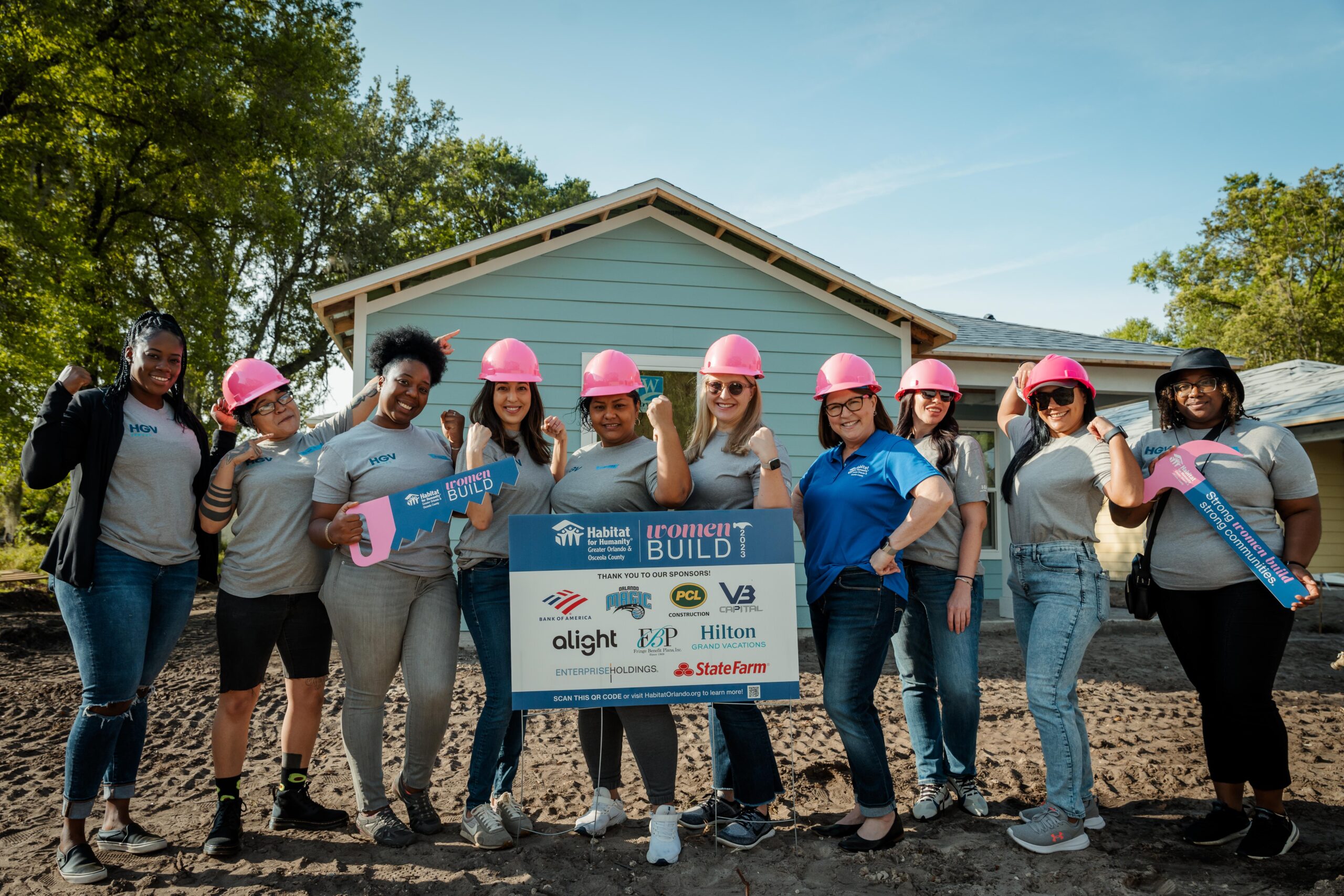 Six people stand in front of a house holding a large check.